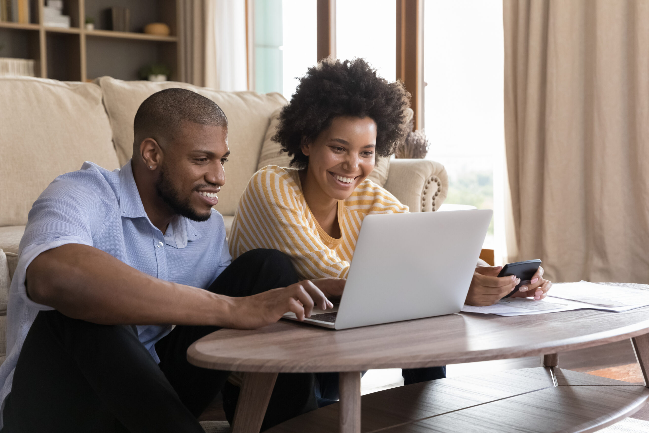 Happy young couple using laptop, looking at screen, smiling